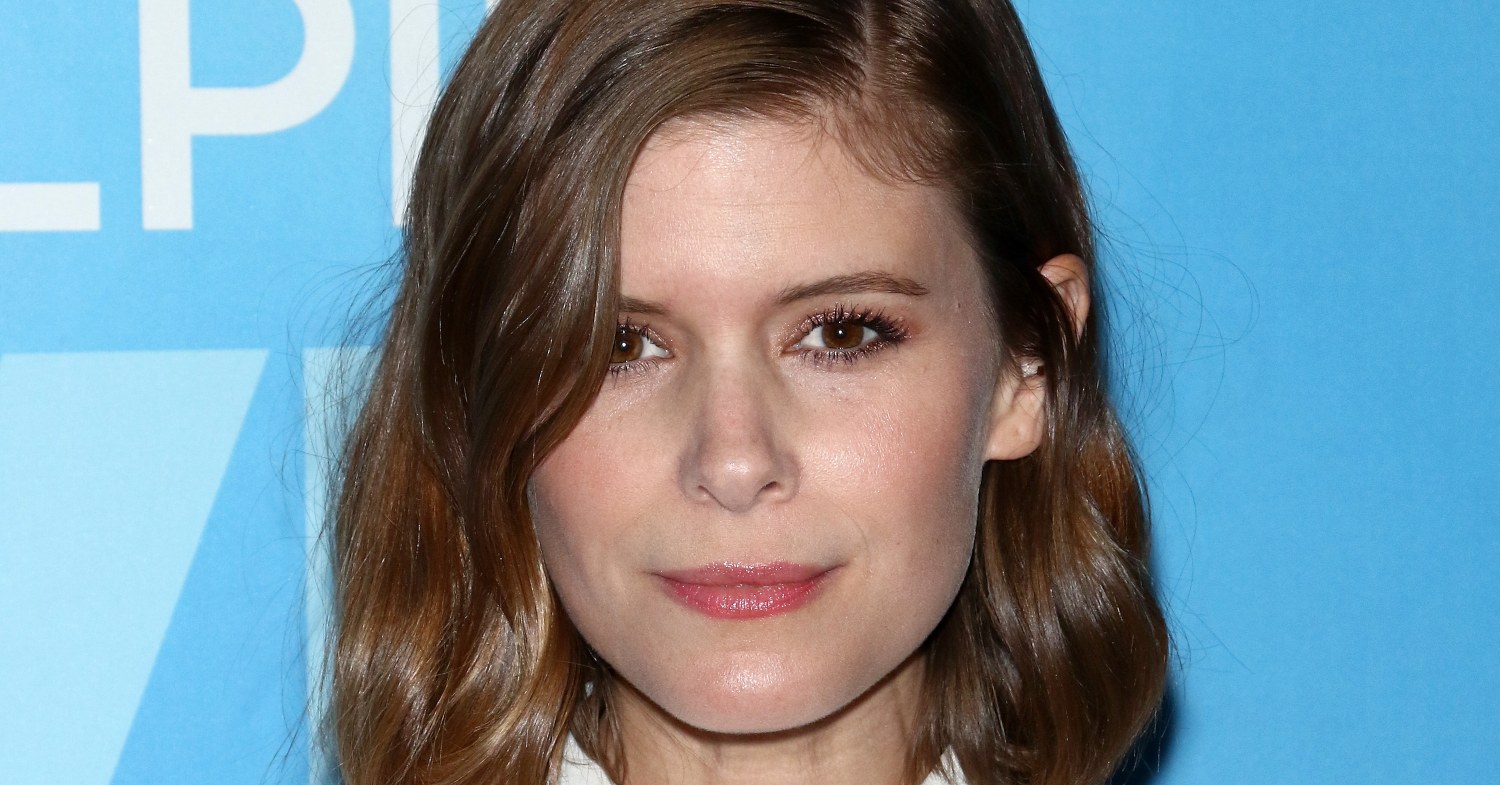 Kate Mara stands against a blue background at an event