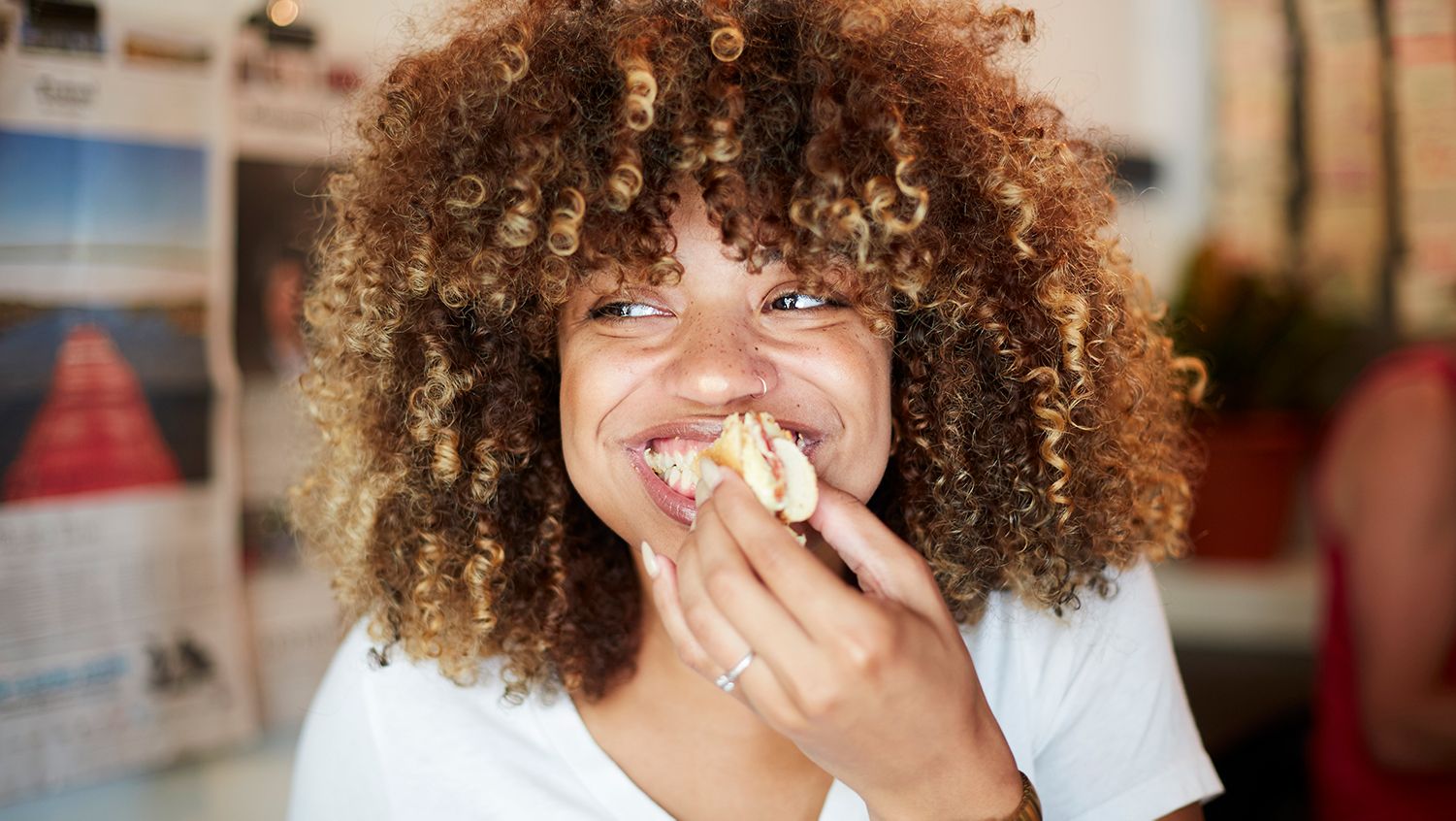 A woman smiles while eating a sandwich