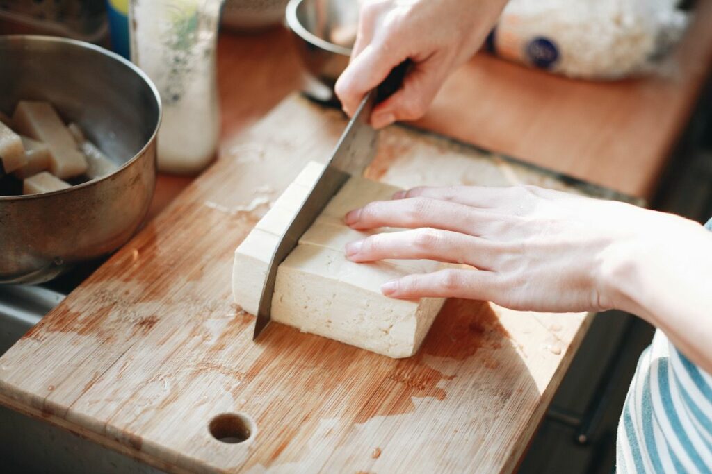 Photo shows a hand cubing a block of tofu with a knife
