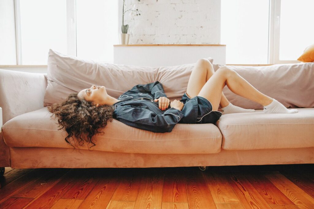 Photo shows a person with long, dark curly hair lying down on a couch with her hands on her stomach.