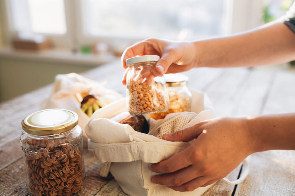 Photo shows someone unpacking glass jars of staple foods such as pasta and lentils.
