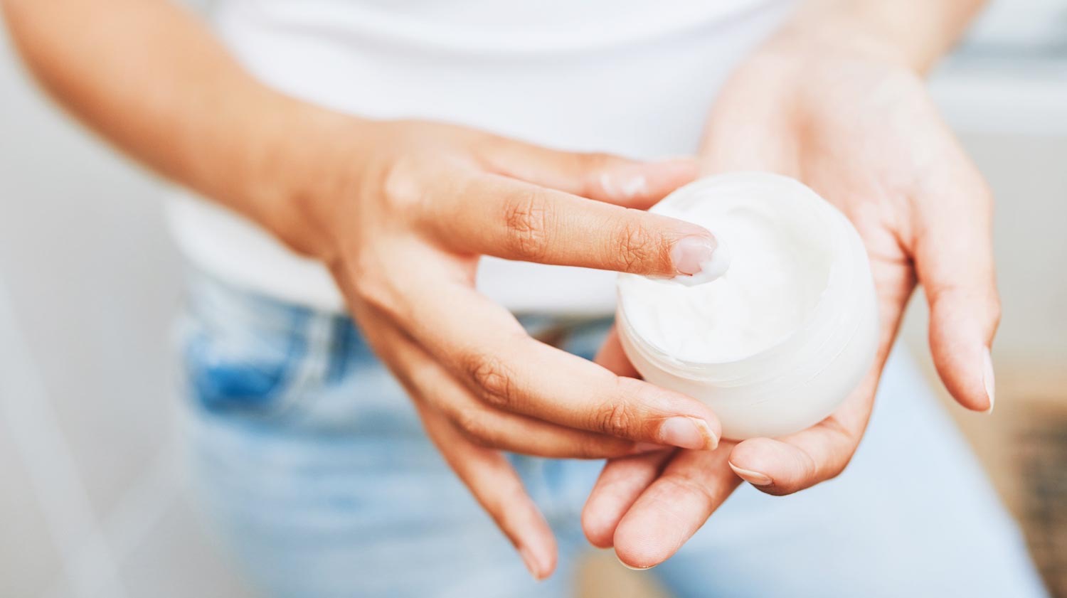 Close up image of a person holding a tub of moisturizer.