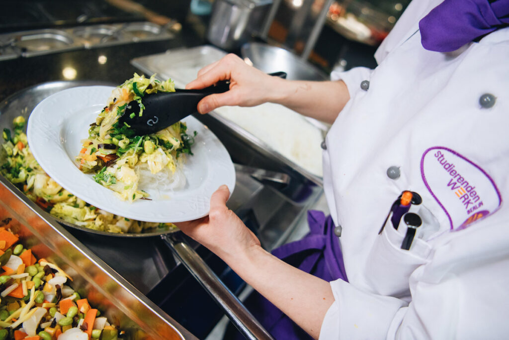 Photo shows cook Nicole Graf serving a vegan dish of glass noodles and Chinese cabbage at Berlin's Technical University, now almost entirely meat-free.