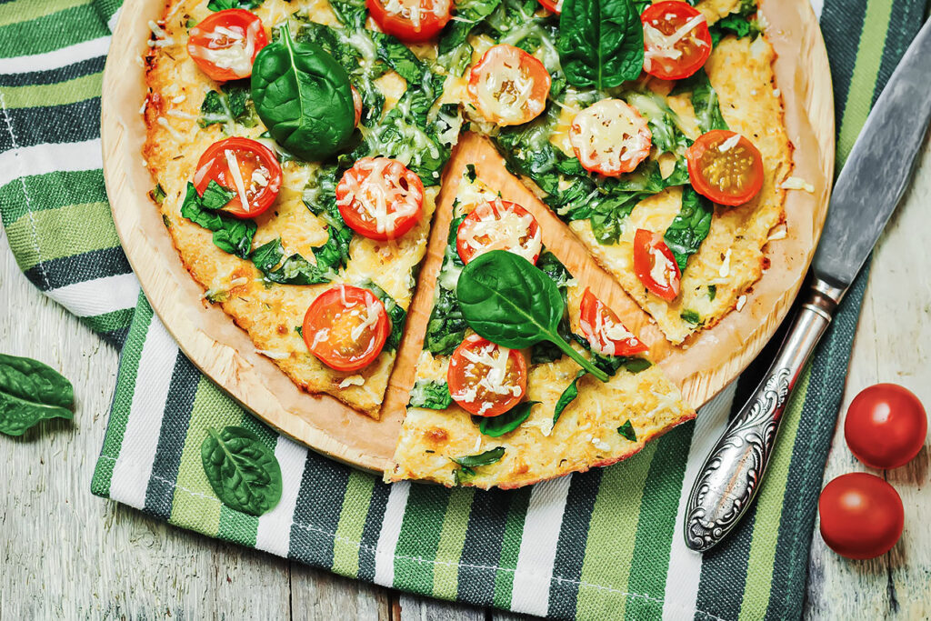 Photo of a light pizza topped with spinach, basil, and tomatos.
