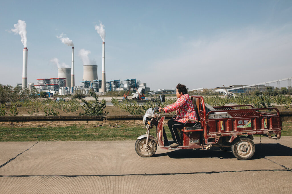 Photo shows someone cycling in Wuhan, China while a coal fired power plant burns in the background.