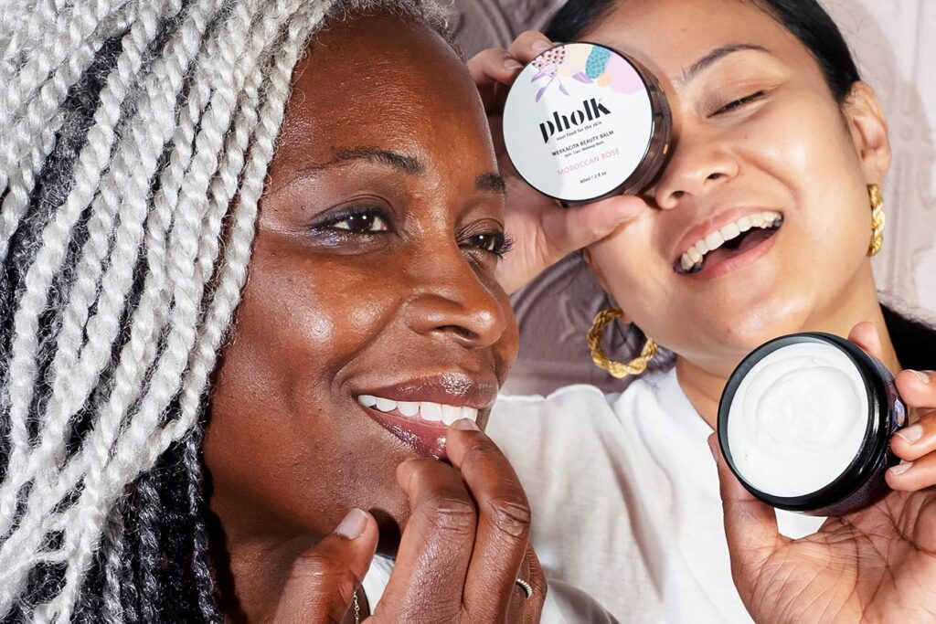 Photo shows a woman with silver twist brands next to a woman wearing gold hoop earrings holding Pholk Beauty's balm.