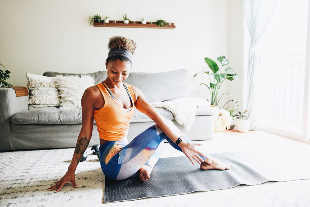 Photo shows a smiling woman stretching on a yoga mat in her living room.
