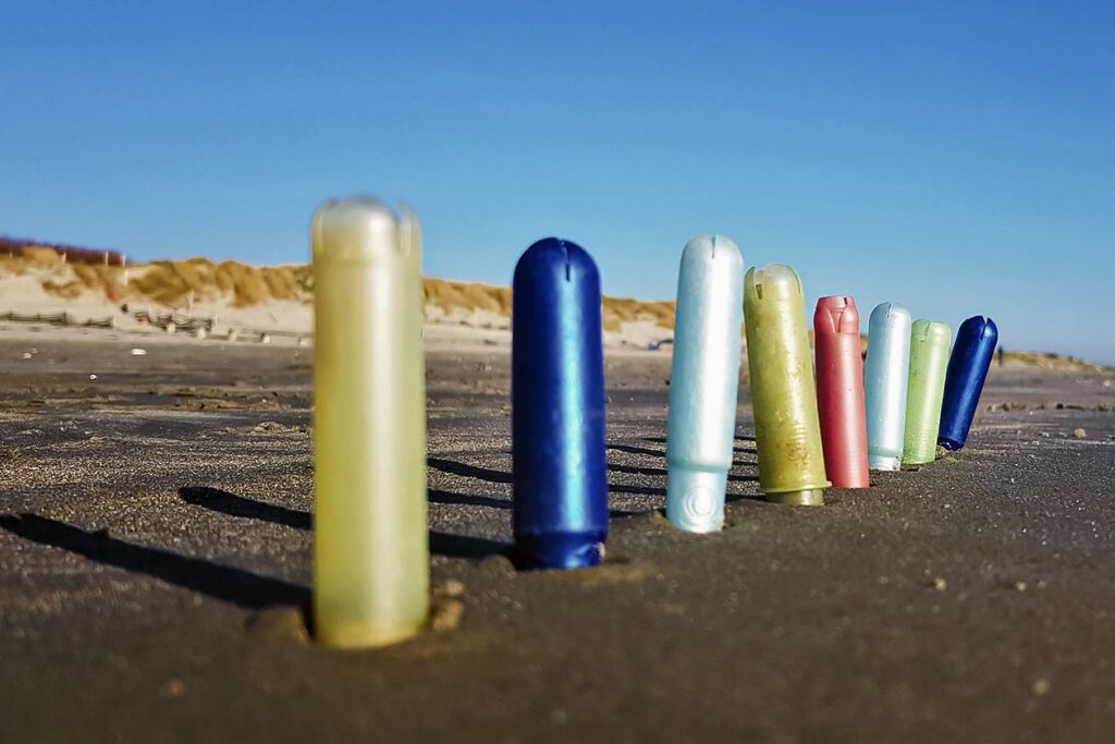 Photo shows discarded tampon applicators lined up on a beach