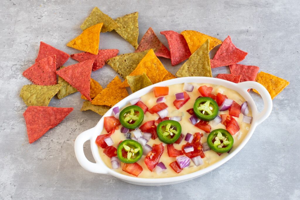 Photo shows vegan queso topped with jalapenos with a side of colorful tortilla chips