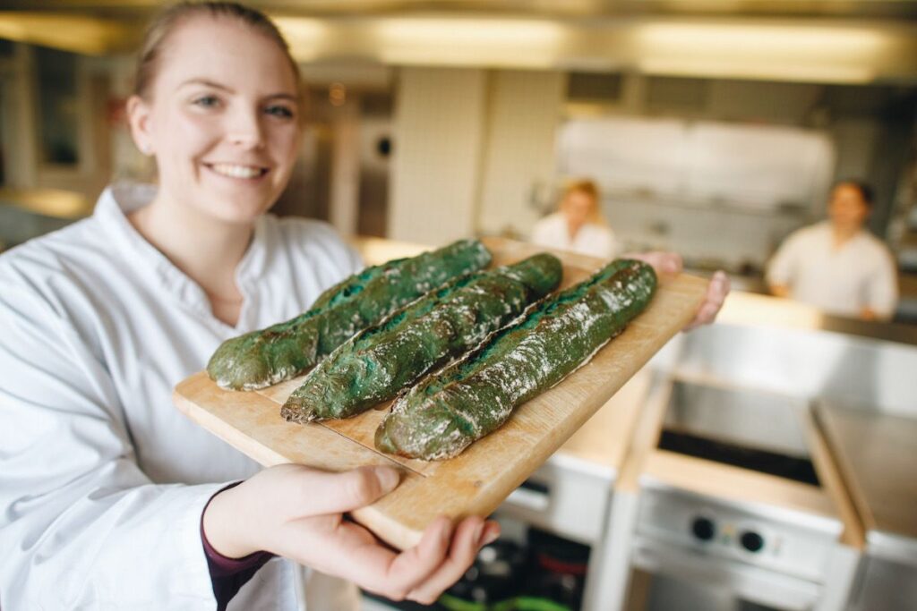 Photo shows a baker holding bread made with algae protein