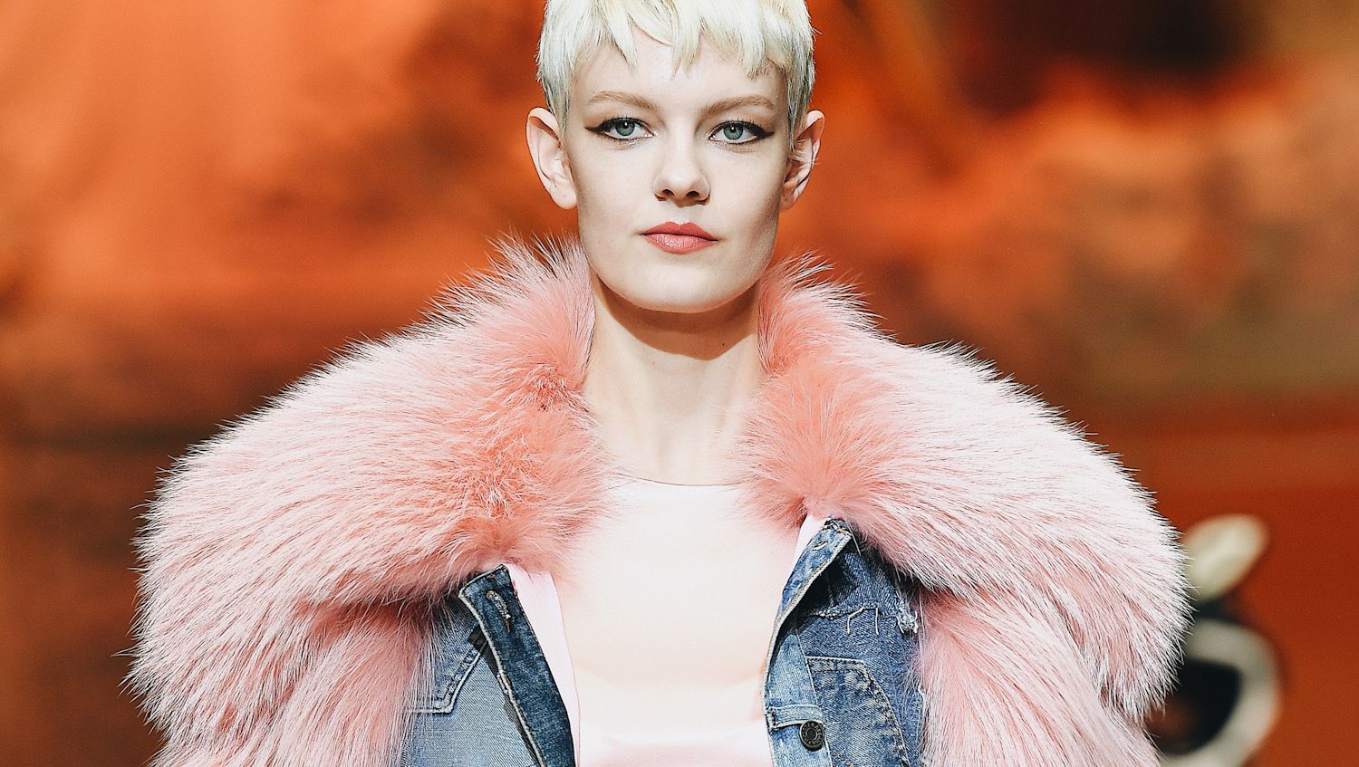 A blonde model with a pixie cut walks the runway at the Dolce & Gabbana show during Milan Fashion Week She is wearing a baby pink fur stole.