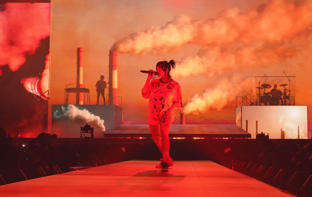 Photo shows Billie Eilish performing in Louisiana last week for her climate positive "Happier Than Ever" world tour. Even the live backdrop features factories pouring pollution.