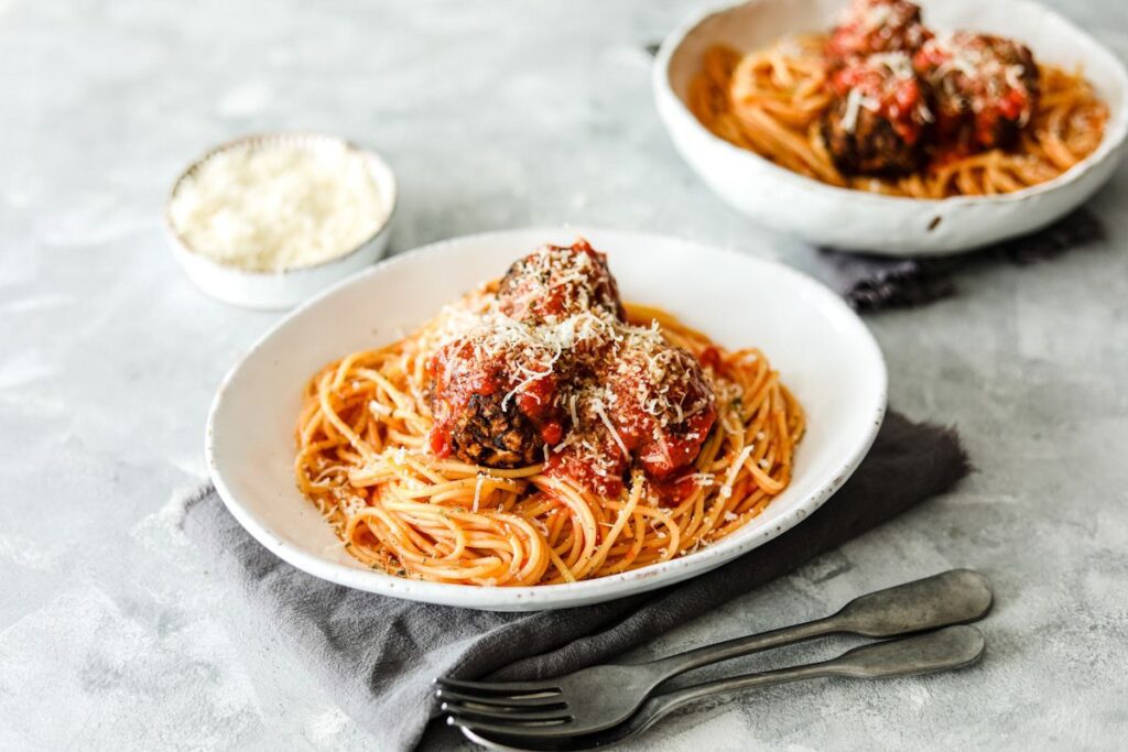 Photo shows a plate of vegan meatballs on top of spaghetti, all covered with cheese