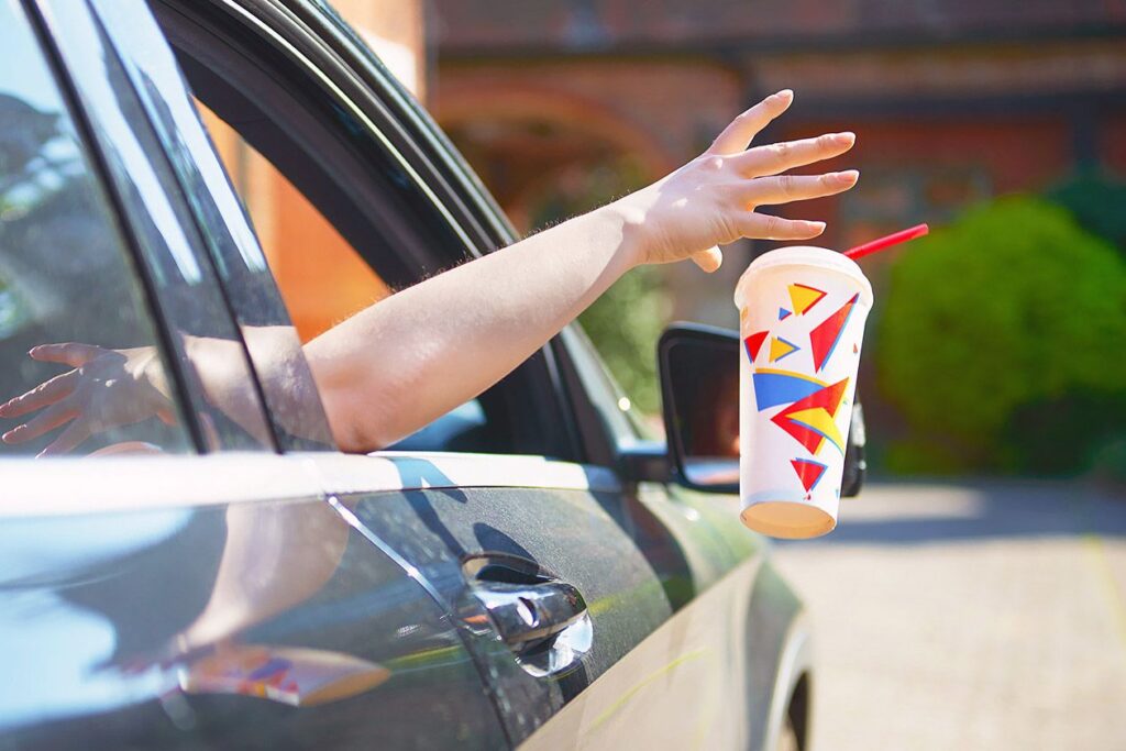 Photo shows a hand throwing a single-use soda cup out of a car window