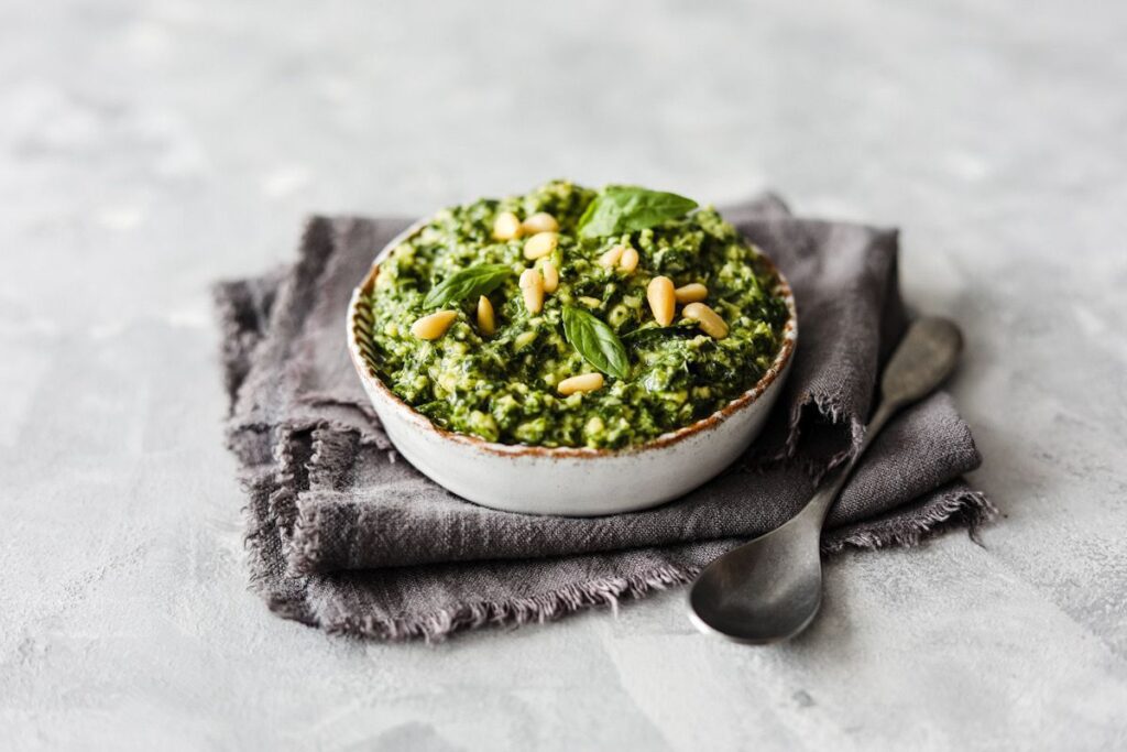 Photo shows a bowl of basil pesto topped with pine nuts
