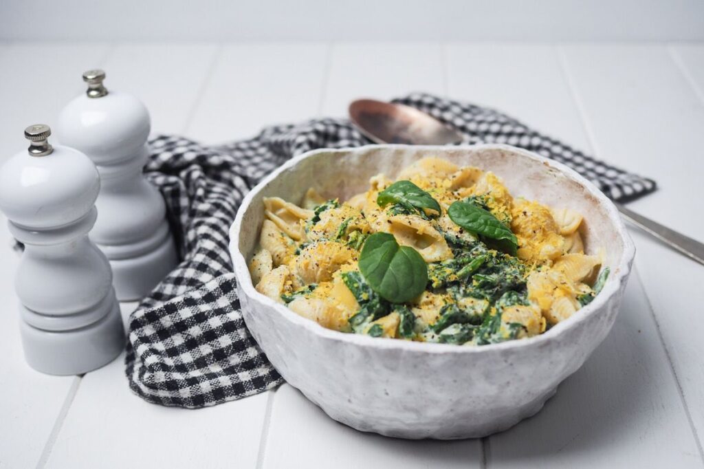 Photo shows a bowl of pasta shells topped with baby spinach leaves